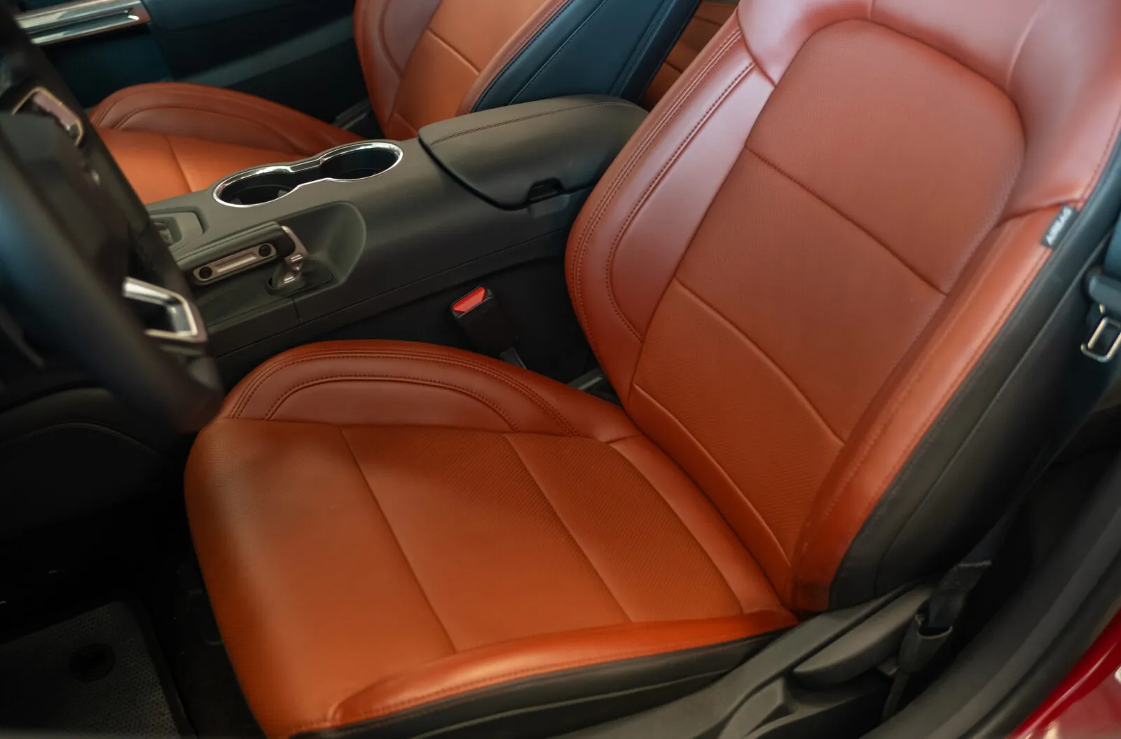 Close-up of a car’s front seats upholstered in brown leather, showing the center console and armrest.