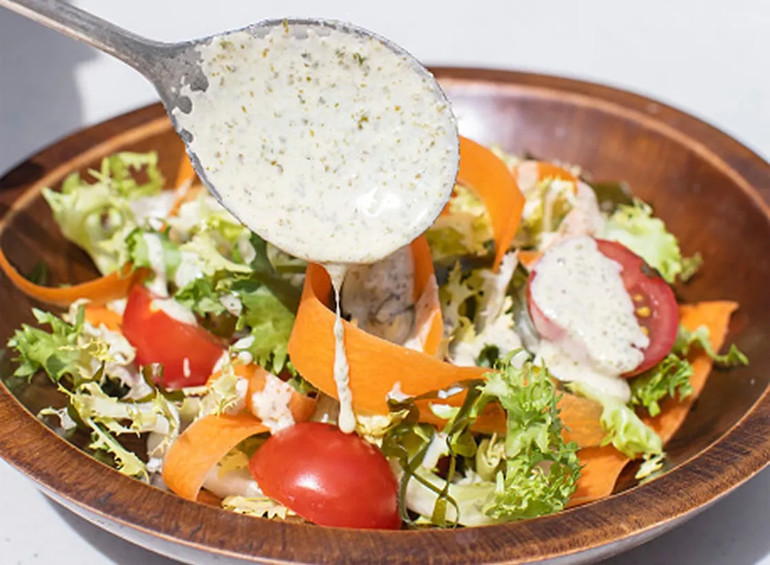 A closeup of salad dressing being poured on a colorful salad.