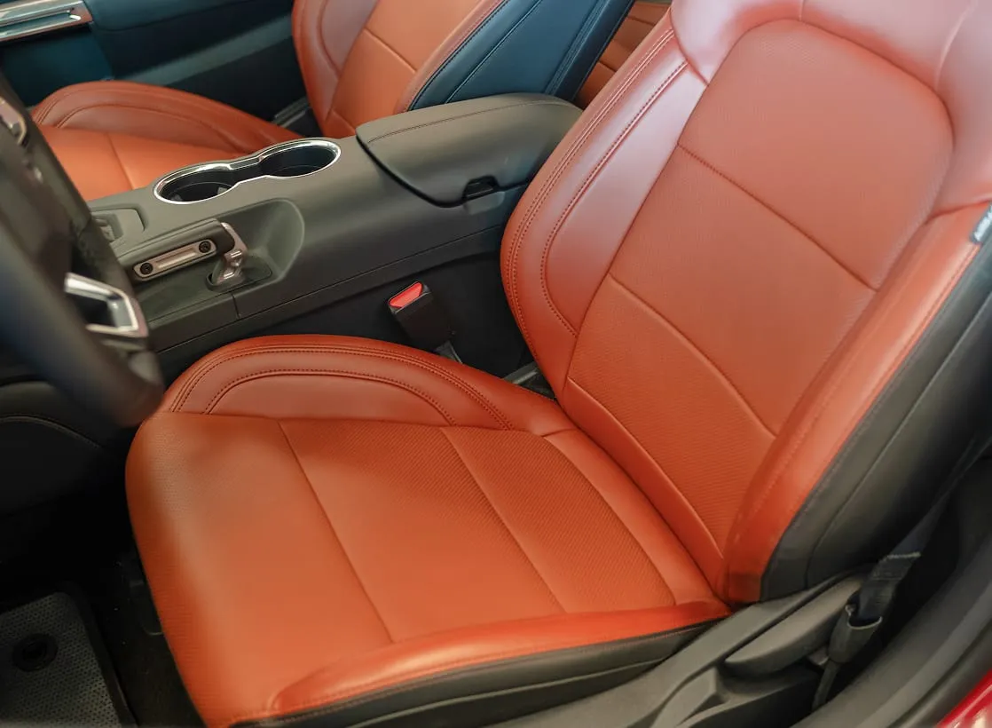 A close-up view of a car’s interior shows smooth, orange-brown leather seats and a central console with cup holders.